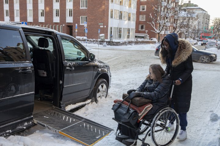 Rullstolsburen kvinna får hjälp att komma in i sin bil av en assistent.